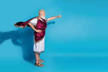 Full body photo of handsome senior male raise fist flying wear ancient greek god king dress isolated on blue color background
