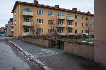Residential apartment buildings in Västerås, Sweden, featuring a Scandinavian architectural style with yellow facades, balconies, and a fenced courtyard in an urban neighborhood setting