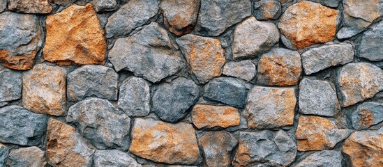 Fototapeta premium Textured stone wall featuring a mix of gray and orange stones arranged in a random pattern, ideal for backgrounds and design projects.