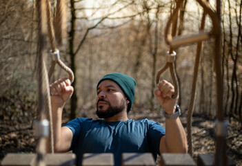 Athletic man in blue shirt and green beanie exercises on outdoor gym equipment surrounded by winter...