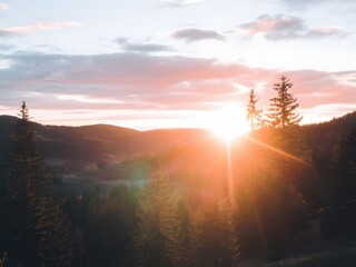 A serene sunrise over a mountainous landscape, with vibrant colors and towering evergreen trees.