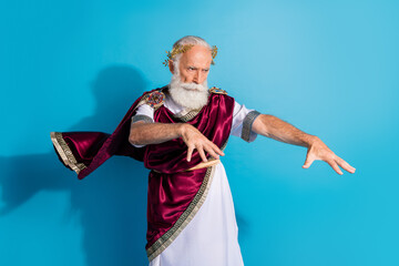 Photo of powerful mature man casting spell wear ancient roman emperor tunic isolated on blue color...