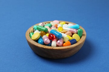 Various pills in a bowl on blue background, top view