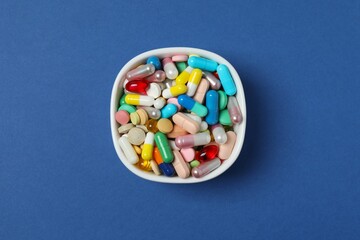 Various pills in a bowl on blue background, top view