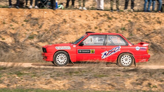 Madrid, Spain; 02-15-2025: Classic red BMW 325i E30 rally car competing on winding dirt roads in a rally under the watchful eyes of the public