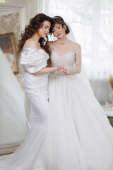Two women in wedding dresses are posing for a picture. One of them is wearing a white dress with a long train. The other woman is wearing a white dress with a long train as well. They are both smiling