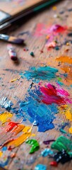 Fototapeta premium A vibrant palette of paint splatters on a wooden surface, showcasing a variety of colors and artist tools, capturing the essence of creativity.