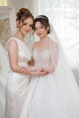 Two women are posing for a picture, one of them is wearing a wedding dress. The other woman is...
