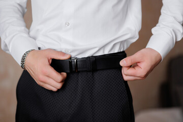 A man is wearing a black belt and is adjusting it. Concept of formality and attention to detail, as the man is making sure his belt is properly fastened