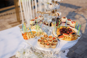 A table with a variety of food and drinks, including cakes, fruit, and wine glasses. The table is set for a party or gathering, and the atmosphere is festive and inviting