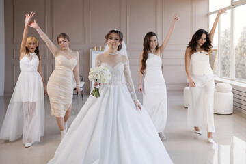 A group of women are posing for a picture in front of a bride. The bride is wearing a white dress...
