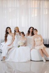 Naklejka premium A group of women are posing for a photo in a room with white curtains. They are all wearing white dresses and are sitting on a couch. One of the women is holding a bouquet of flowers