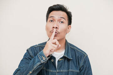 A Southeast Asian man wearing a denim jacket with Funny face putting his fore finger in his lips...