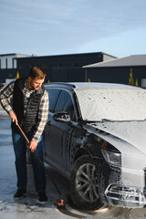 Naklejka premium Car wash equipment. A man is washing a car at self service car wash. High pressure vehicle washer machine sprays foam