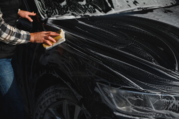 A man washes a car with a sponge at a self-service car wash