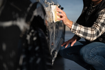 A man washes a car with a sponge at a self-service car wash