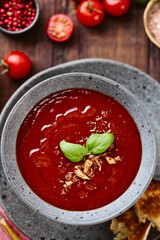 Thick rich Tomato puree Soup garnished with basil leaves and spices in bowl with Grilled Croutons on dark wooden table