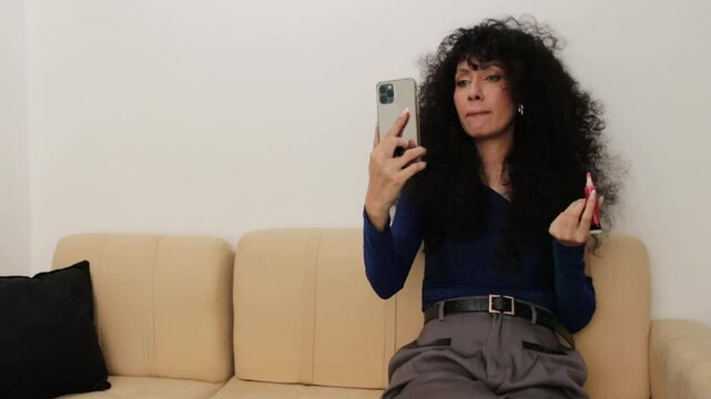 Video of a Latina woman looking at her cell phone screen while applying lipstick