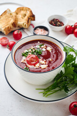 Tomato puree soup garnished with parsley, feta cheese and spices with toasted bread slices, tomatoes and herbs on white table