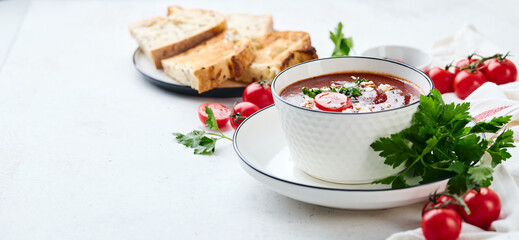 Tomato puree soup garnished with parsley, feta cheese and spices with toasted bread slices, tomatoes and herbs on white table