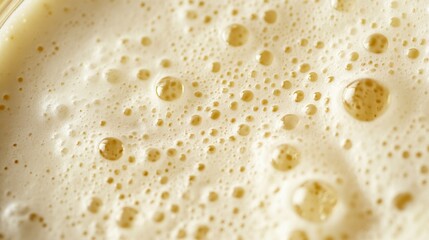 A macro shot displaying foam bubbles on a creamy, light-colored liquid surface. The abstract texture and golden hues of the foam create a visually appealing image ideal for food or drink-related