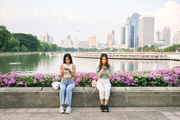 Obraz premium Two young women using smartphones in bangkok park