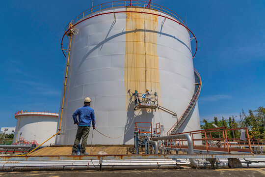The male worker takes the cable car holding an industrial painting white color brush used for shell plate tank oil surface