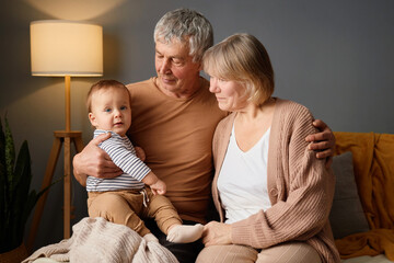 A loving grandparents hold their grandson in a warm and inviting living room. Soft lighting...
