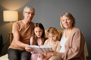A warm afternoon is spent as grandparents sit with their two grandchildren on a couch, enjoying a book together in a cozy living space filled with soft lighting