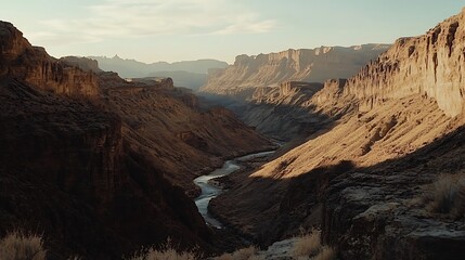 Obraz premium Golden hour sunlight illuminates a deep canyon with a river winding through it.