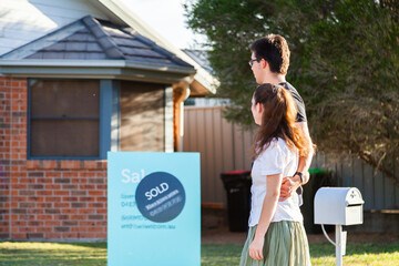 Young couple looking at front of suburban house with sold sign