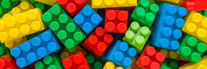 Background of heap colorful plastic blocks. Closeup. Wide banner. Top down view.