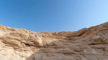 Fototapeta premium A rocky cliff with a blue sky in the background. The sky is clear and bright, and the rocks are jagged and rough. The scene is peaceful and serene