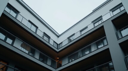 Obraz premium A modern apartment building viewed from below, showcasing geometric lines and balconies against a cloudy sky.