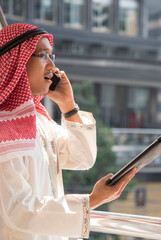 Fototapeta premium Portrait Vertical Islamic man smile look at camera wear muslim dress in modern uae city. Vertical horizon Arab men wear hijab Headscarf muslim formal dress lifestyle. Arabman saudi Arabian Culture