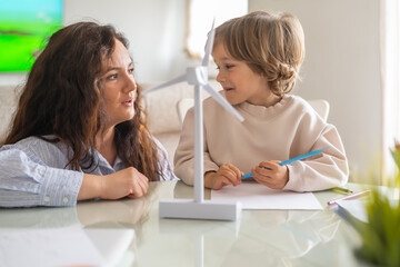 Mother and son learning about renewable energy using a miniature wind turbine model at home, discussing sustainability and environmental awareness