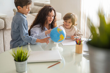 Mother and two sons engaging in geography lessons with a globe and colored pencils at home,...