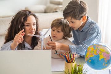 Mother and children learning about renewable energy using a small wind turbine model, colored pencils, a world globe, and a laptop, promoting stem education and environmental awareness © Nanci