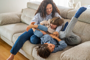 Happy family enjoying free time together at home, mother tickling and playing with her two cheerful...