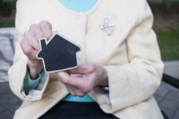 Close-up senior woman wrinkled hand holding a house, home, sell, buy. Horizontal. Faceless.	