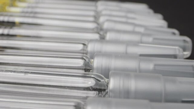 Close-up of disposable syringes for vaccinations or subcutaneous injections. The reflective black surface enhances the sharp details of the glass and needles.