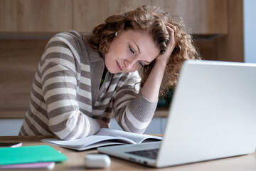 Tired female difficulty concentrating while working on laptop. Exhausted woman with low hemoglobin, burnout holding head in chronic fatigue, looking at documents feeling mentally, physically drained.