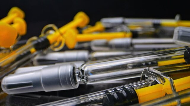 Close-up of disposable syringes for vaccinations or subcutaneous injections. The reflective black surface enhances the sharp details of the glass and needles.