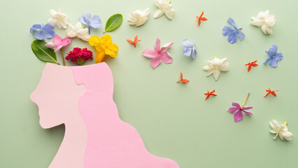 Mental Health Awareness Month. Woman head with colorful fresh flower on green background. Peace of...
