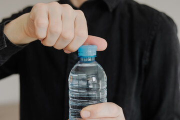 Close-up of man opening the plastic cap of water bottle. Daily water intake.