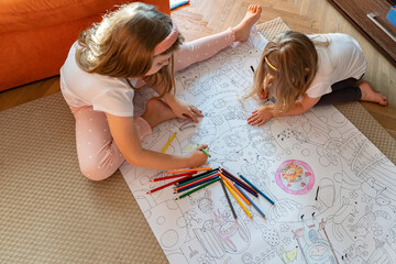 Children girls draw on a large sheet of paper, coloring with colored pencils. Hobby, learning,...