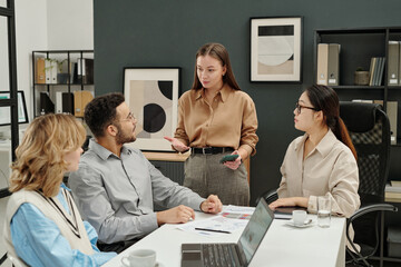 Portrait of young businesswoman as female boss talking to team of colleagues while leading business...