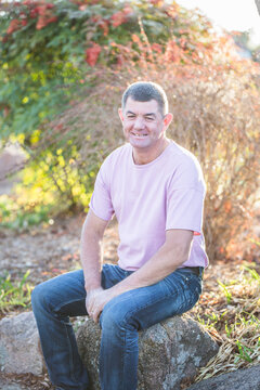Man in 50s sitting on rock in garden smiling with dimples