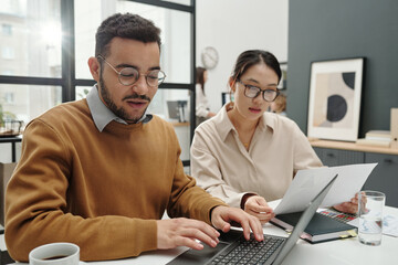 Obraz premium Portrait of young Middle eastern man working with female colleague in meeting and using laptop in office