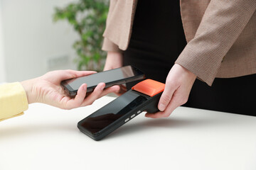 Woman paying for service with smartphone via terminal at white table indoors, closeup